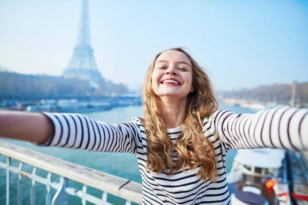 Beautiful young girl taking funny selfie with her mobile phone near the Eiffel tower