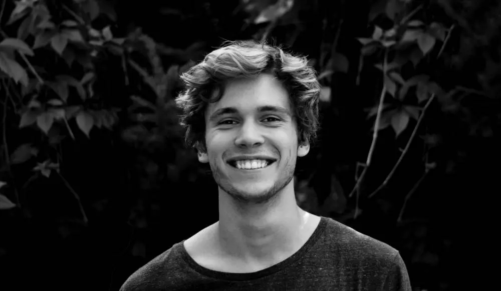 A man smiling for the camera in front of trees.