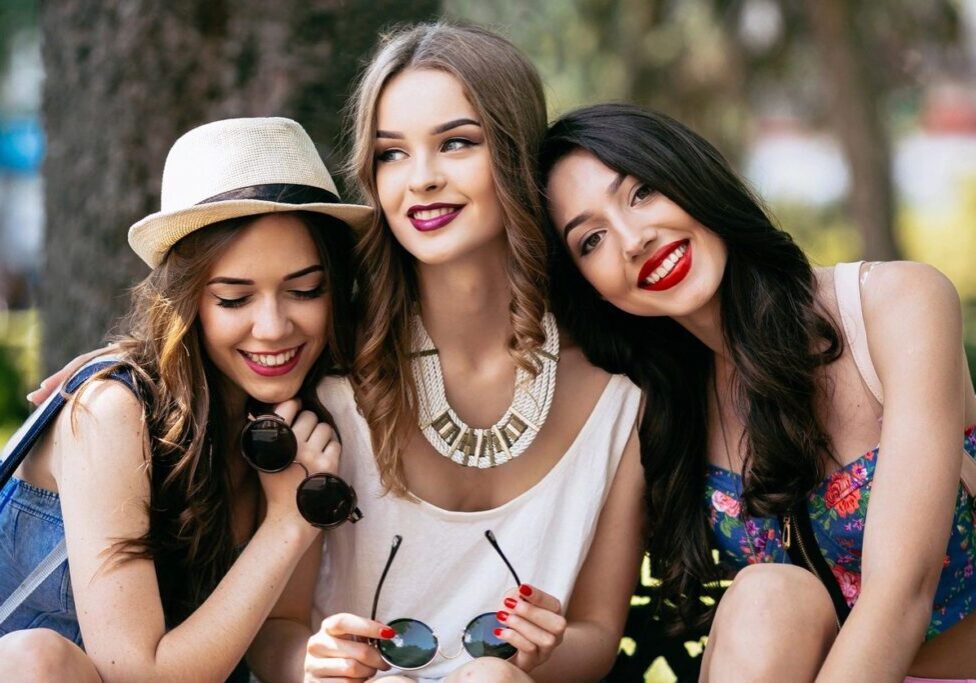 Three women posing for a picture with one wearing a hat and the other wearing sunglasses.